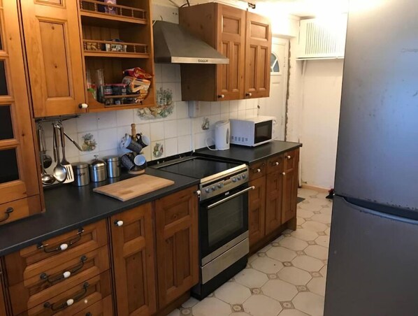 Compact kitchen with a classic design, featuring a stainless steel oven, microwave, and refrigerator, along with a kettle and cutting board.