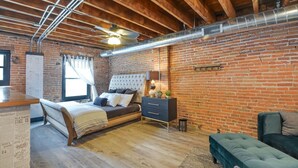 Een slaapkamer met houten plafond, bakstenen muren, een bed, een kapstok en een raam.