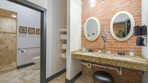 A bathroom with a brick wall, two mirrors, a sink with a granite countertop, and a toilet. - Elle & Beck`s 2 story suite (Galena)