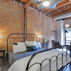 A room with exposed brick walls, a metal bed frame, a small bedside table, and a hanging light fixture. - Elle & Beck`s 2 story suite (Galena)
