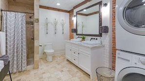 A bathroom with a shower, toilet, double sink vanity, large mirror, and a front-loading washing machine. - Elle & Beck`s 2 story suite (Galena)