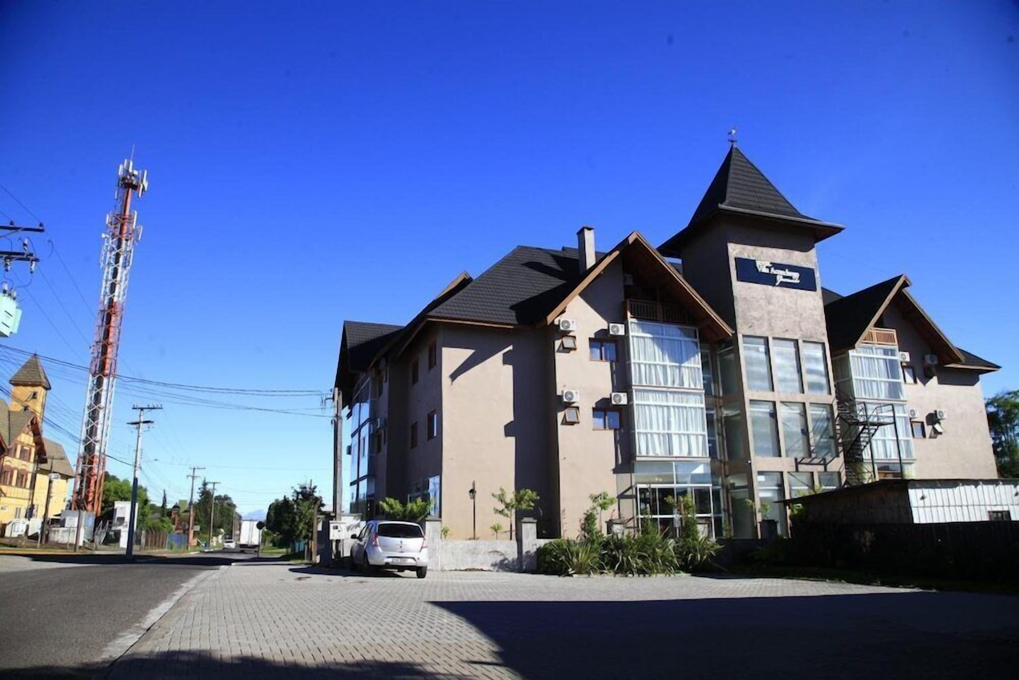 A two-story building with a prominent tower-like structure on the left, a large glass entrance on the right, and a parking area in front.