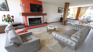 A modern living room with a fireplace, grey sofas, and a dining area. - Hotel Villa Aconchego de Gramado (Gramado)