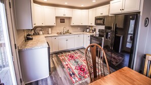 Una cocina con armarios blancos, un refrigerador de acero inoxidable y una mesa de comedor de madera.