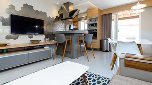Een moderne keuken met een flatscreen televisie, een centraal eiland met barkrukken, en een eethoek met een witte tafel en stoelen.