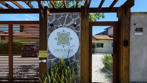 Een poort met een stenen muur, een houten pergola en een bord met de naam 'Cor de Buzios'.