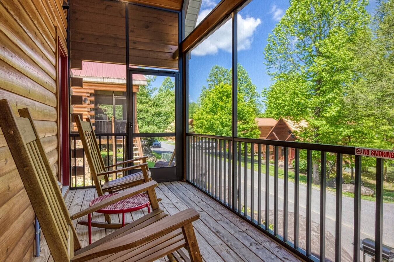 A wooden deck with chairs and a red chair, a balcony with a railing, and a view of a road and trees.