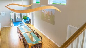 Un comedor amplio con una larga mesa de madera y sillas, un sofá azul y vistas al exterior a través de una ventana.