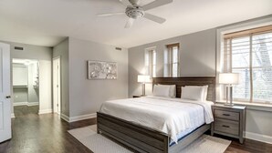 Un dormitorio con cama, mesitas de noche, ventilador de techo y ventana con persianas.
