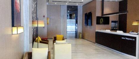 Un hall d’hôtel moderne avec un comptoir d’accueil, un espace salon et une grande fenêtre.