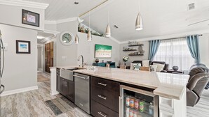 A modern kitchen with a large island, stainless steel appliances, and a refrigerator with beverages.