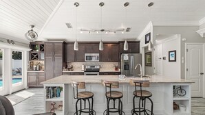 A modern kitchen with a large island, bar stools, and pendant lighting.