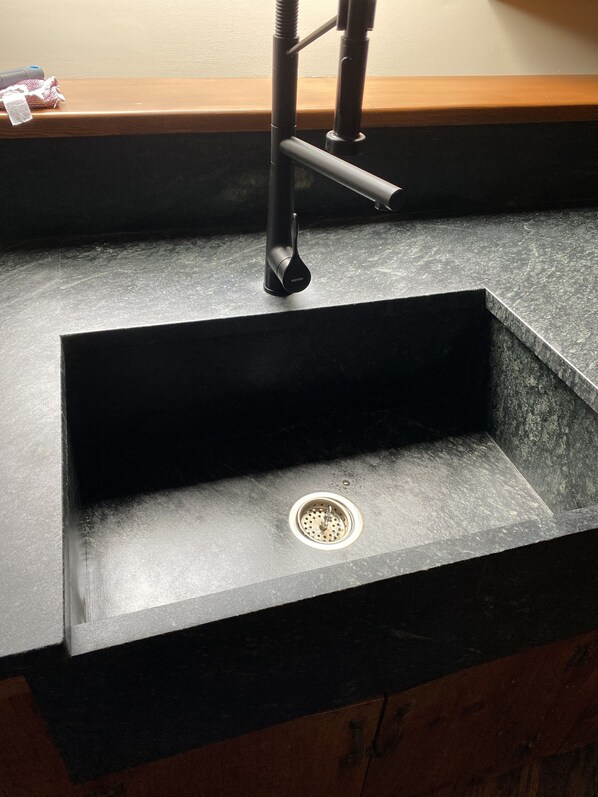 A modern kitchen sink with a black countertop and a stainless steel faucet.