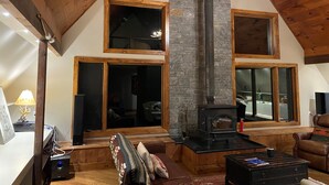 Una sala de estar acogedora con chimenea de piedra, vigas de madera y ventanas amplias.