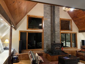 A cozy living room with a stone fireplace, wooden beams, and large windows.