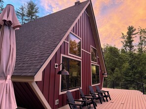 A red wooden cabin with a sloped roof, large windows, and a deck with chairs.