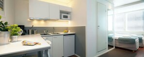 A compact kitchen with a microwave, sink, and a small refrigerator. There is a dining area with a white table and chairs. - Forenom Aparthotel Helsinki Kamppi (Helsinki)