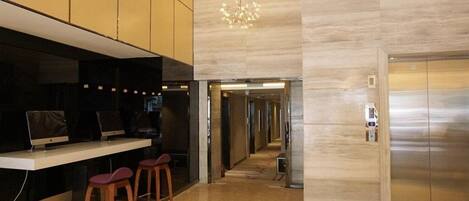 A modern lobby with a reception desk, bar stools, a chandelier, and an elevator.