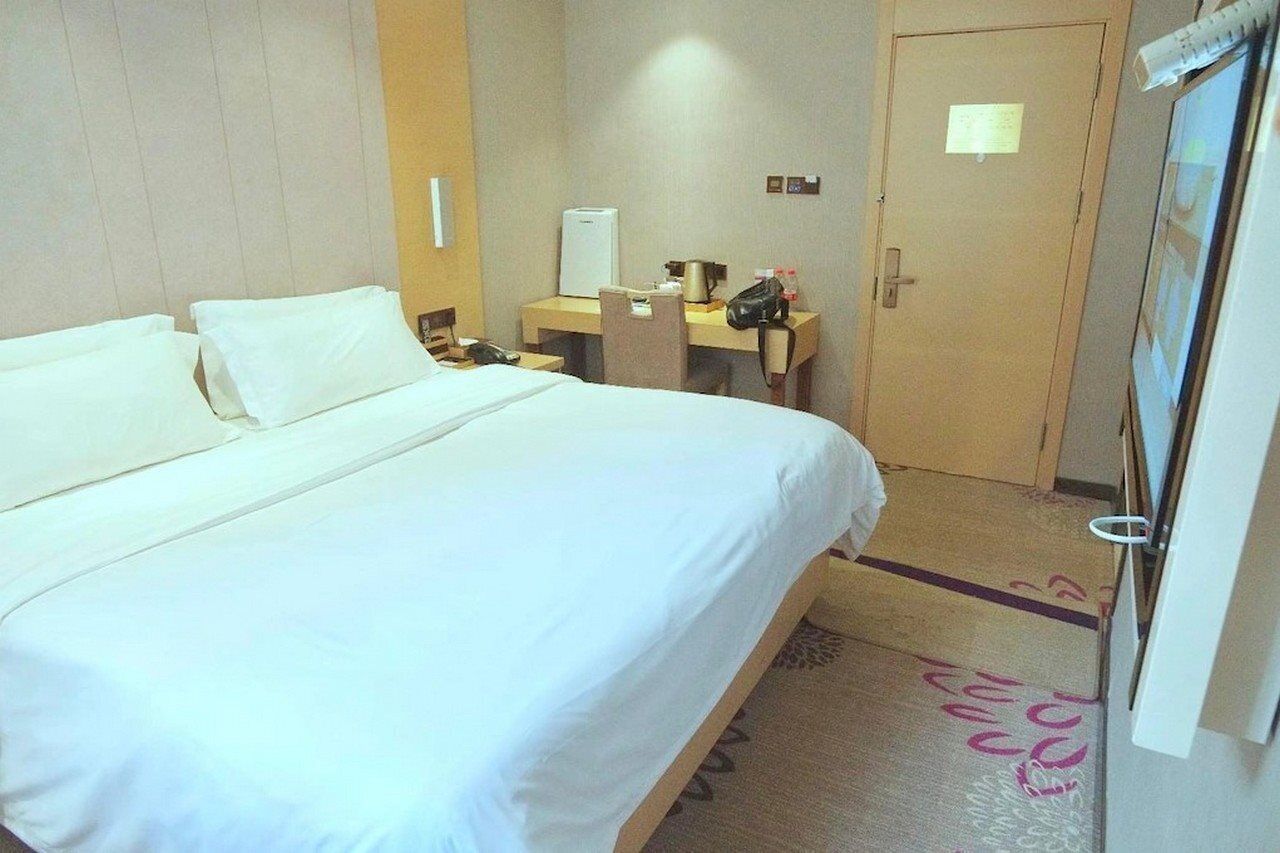 A hotel room with a large bed, a desk with a computer, a chair, a telephone, and a door.