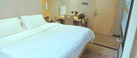 A hotel room with a large bed, a desk with a computer, a chair, a telephone, and a door.