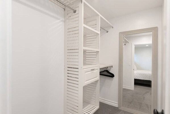 A walk-in closet with open shelving and a hanging rod, a mirror, and a door leading to a bedroom with a bed. - Ocean View Escape_3Bd, 2 Ba, Private Spa and Views (San Clemente)