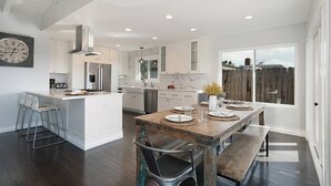 A spacious kitchen with white cabinetry, a central island, and a dining area with a rustic wooden table.