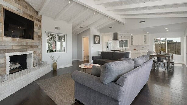 A spacious living room with a fireplace, grey sofa, and a dining area with a table and chairs.