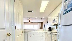 A kitchen with white cabinets, a wooden floor, and a refrigerator. - Beachfront Condo, Gulf Views, Sunset Balcony, Okaloosa Island (Fort Walton Beach)