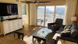 A living room with a television, a ceiling fan, a sofa, a coffee table, and a view of the outdoors. - Beachfront Condo, Gulf Views, Sunset Balcony, Okaloosa Island (Fort Walton Beach)