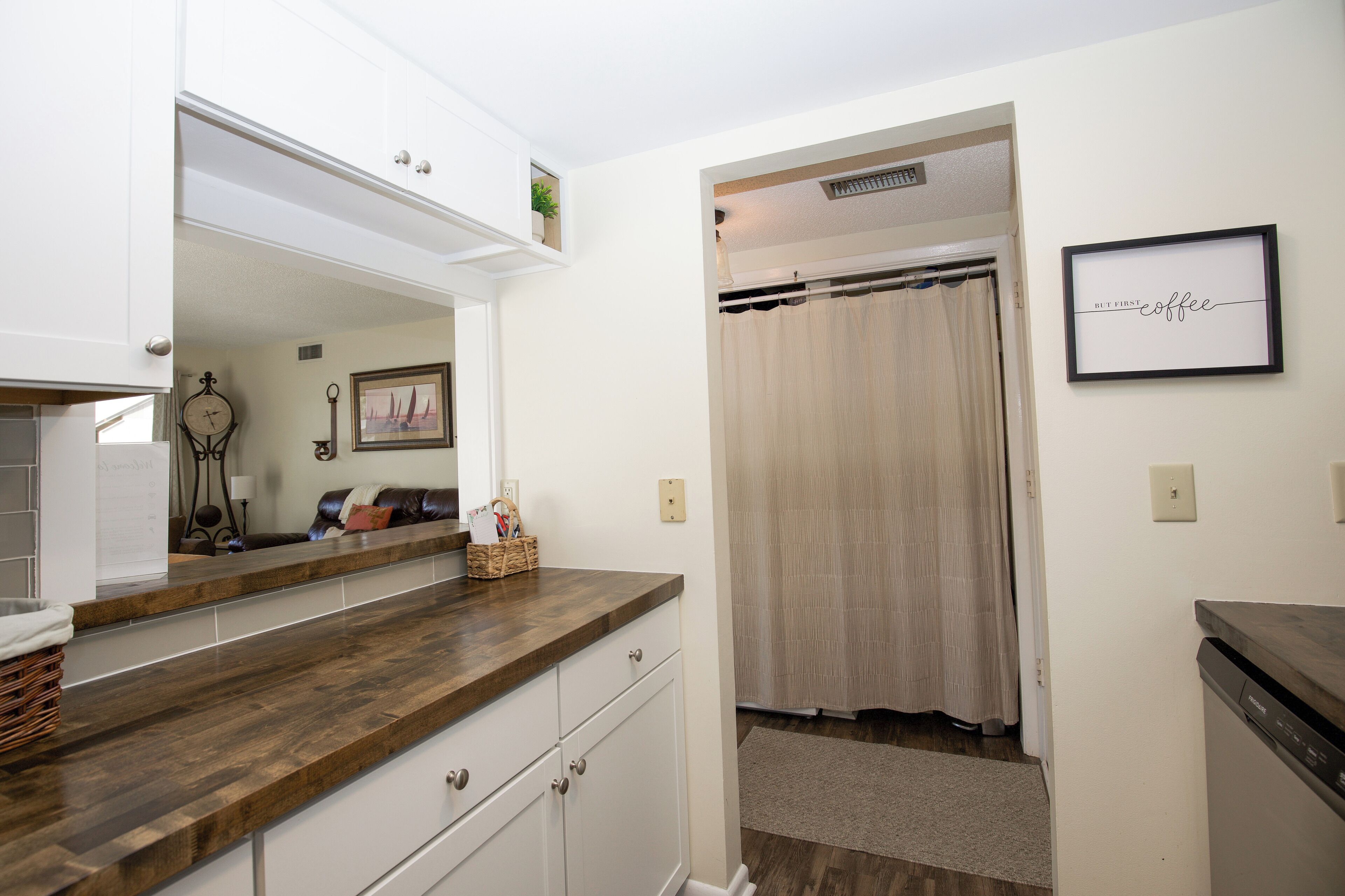 A kitchen with a wooden countertop, white cabinets, and a framed picture on the wall.