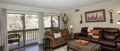 A living room with a brown leather sofa, a small table with a tray, a clock, and a framed picture on the wall.