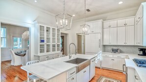 A modern kitchen with white cabinetry, a central island, and pendant lighting. - Charming WaterColor Home: Bikes, 6 Seater Electric Cart, Outdoor Fireplace, Steps to Camp WC! (Santa Rosa Beach)