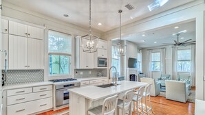 A modern kitchen with white cabinetry, a central island with bar stools, a microwave, and a gas stove. - Charming WaterColor Home: Bikes, 6 Seater Electric Cart, Outdoor Fireplace, Steps to Camp WC! (Santa Rosa Beach)