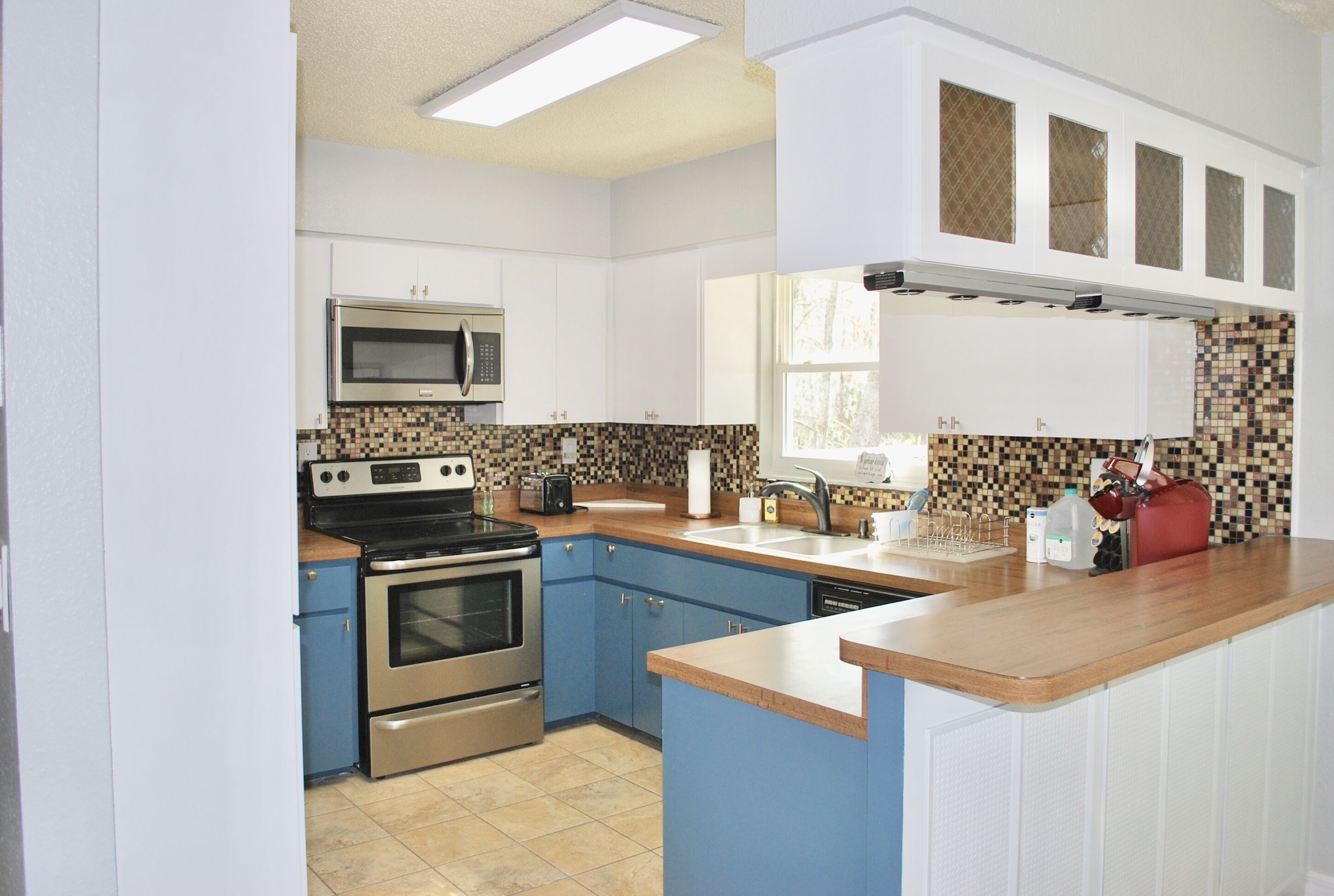A kitchen with white cabinets, a microwave, a stove, and a tiled backsplash.