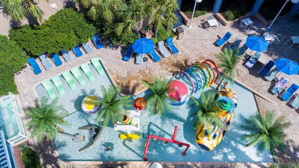An aerial view of a resort's pool area with multiple water slides, lounge chairs, and palm trees. - Partial Ocean Views in South Myrtle Beach - Full Access to Amenities! (Myrtle Beach)