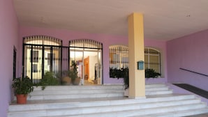 Entrada de un edificio con escalones que llevan a una puerta, una columna y plantas en macetas.