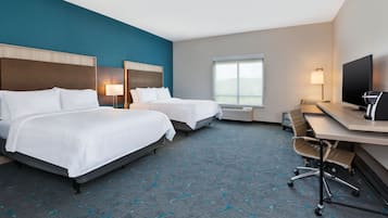 Quarto de hotel com duas camas, uma escrivaninha, uma televisão e uma janela.