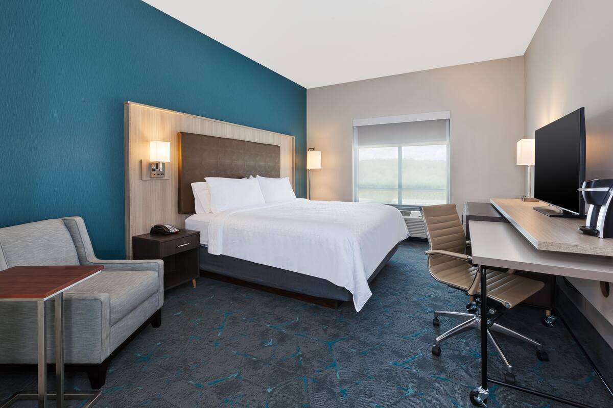 A hotel room with a bed, a desk, a chair, a TV, and a window.