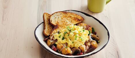 A bowl of food with toast and scrambled eggs on a wooden table.