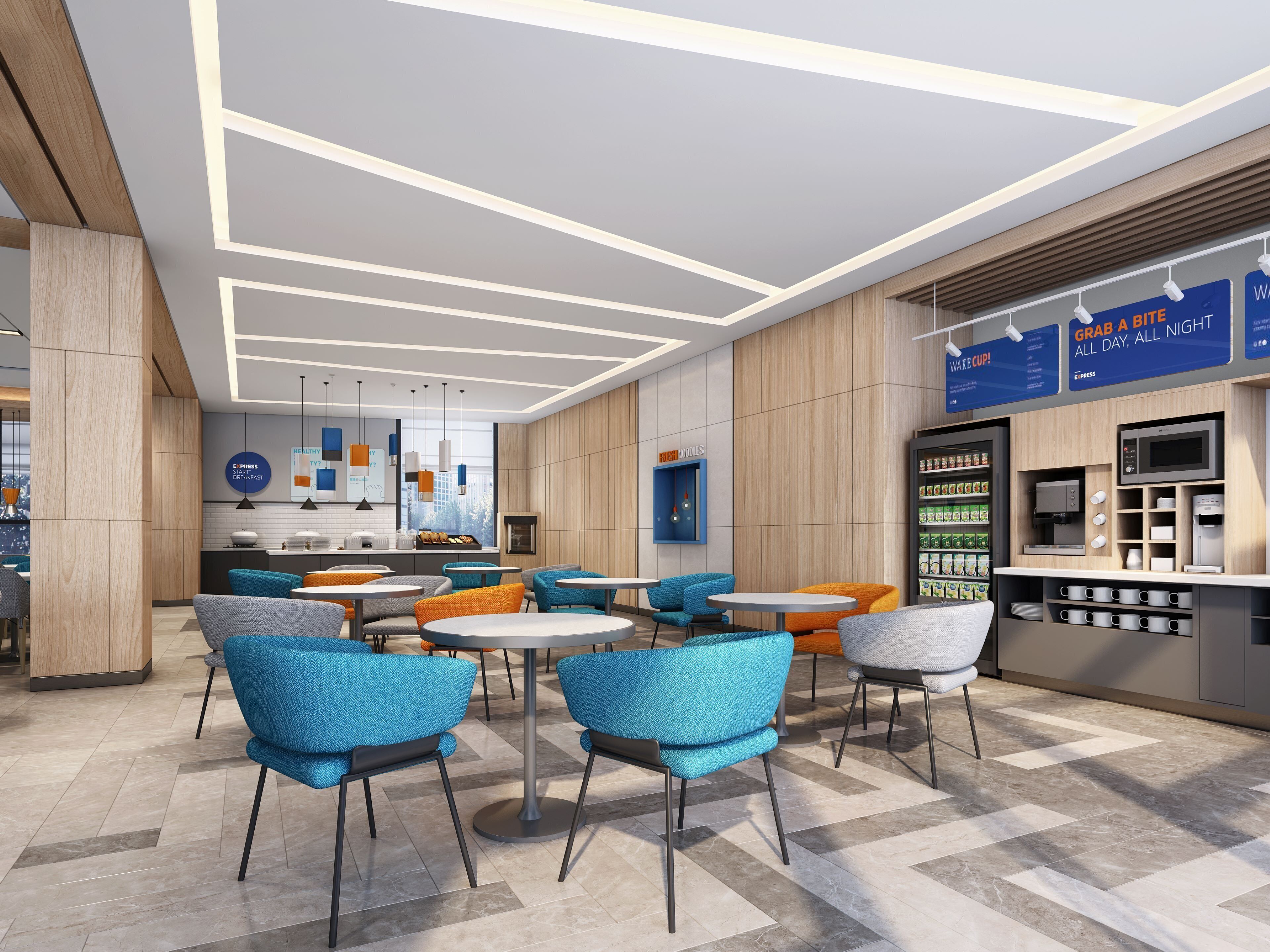 A modern cafe with round tables and blue chairs, a coffee machine, and a menu board advertising grab-and-go options.