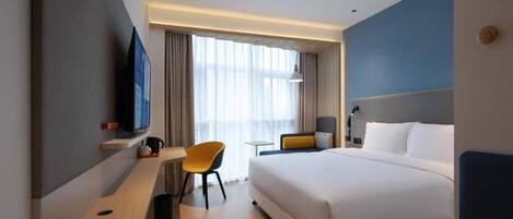A modern hotel room with a large bed, a desk with a chair, a TV, and a window with curtains.