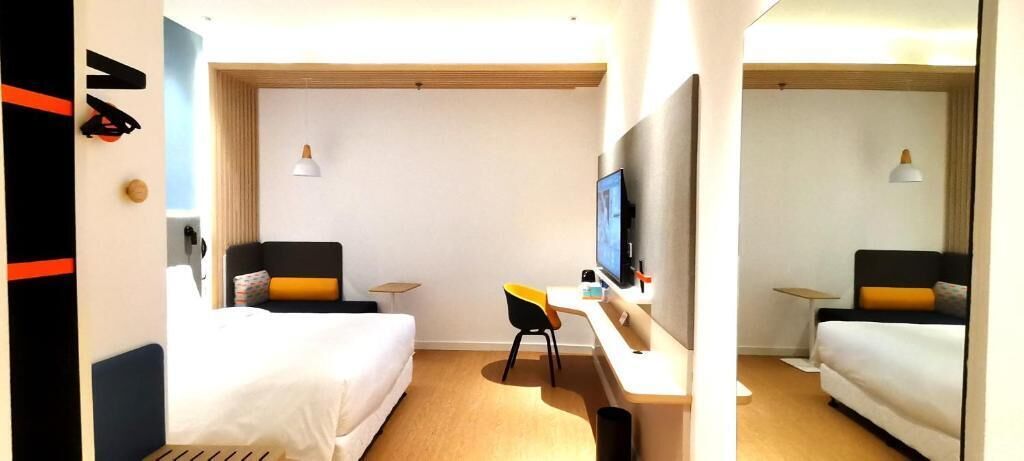 Quarto de hotel com duas camas, uma escrivaninha, uma TV e uma mesinha.