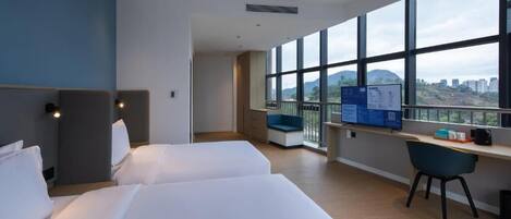 A hotel room with two beds, a desk, a chair, and a large window offering a city view.