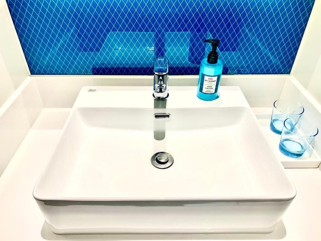 A bathroom sink with a blue tiled backsplash, a faucet, a soap dispenser, and two glasses.