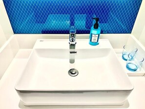 Een wastafel met een blauwe betegelde spatwand, een kraan, een zeepdispenser en twee glazen.