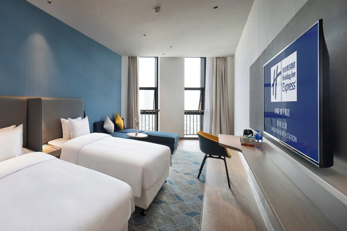 Een hotelkamer met twee bedden, een bureau, een stoel en een groot televisiescherm waarop het logo van Holiday Inn Express staat.