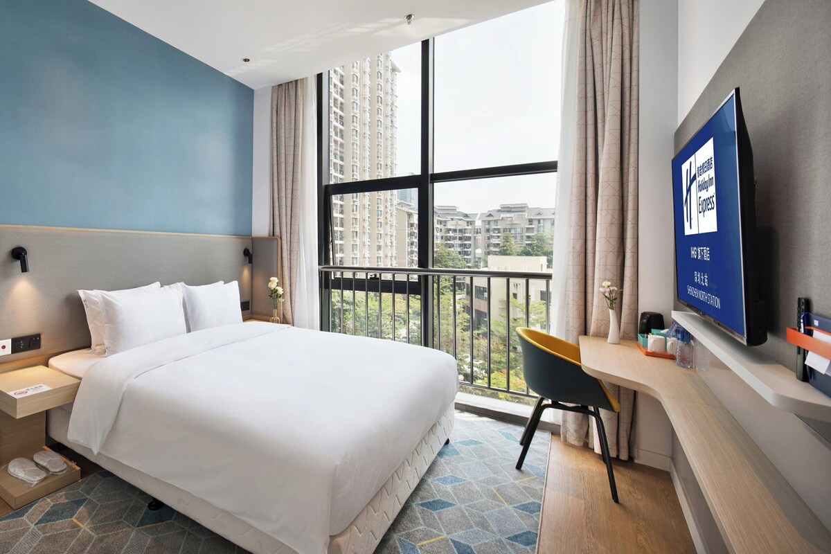 Hotelkamer met een groot bed, een bureau met stoel, een televisie en een raam met uitzicht over de stad.