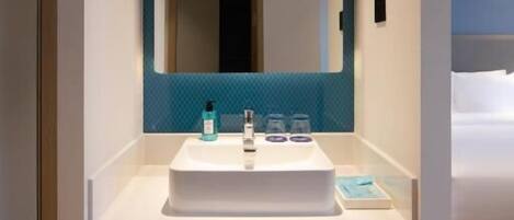 Une salle de bain moderne avec un lavabo blanc, un mur recouvert de carreaux bleus et un grand miroir. Deux serviettes blanches sont suspendues sur un porte-serviettes situé sous le lavabo.