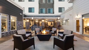 Un espace patio extérieur moderne, doté d’un foyer central et entouré de meubles en osier.