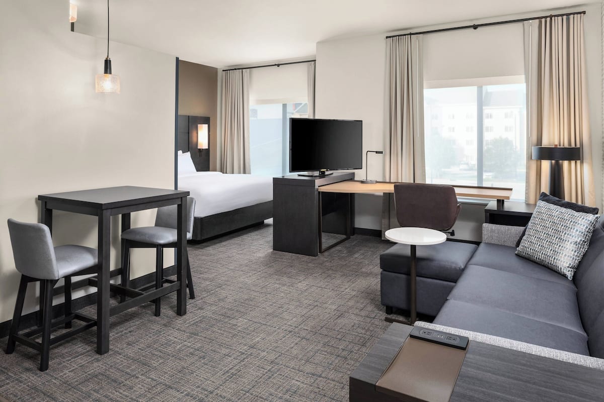 A modern hotel room with a bed, a desk with a computer, a sofa, and a TV.